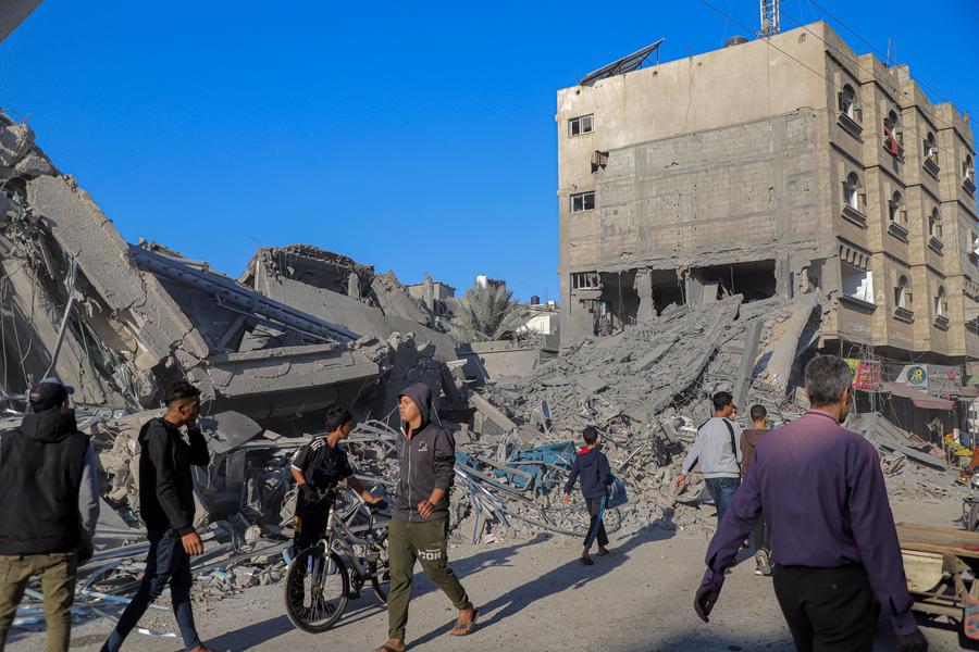 지난 17일(현지시간) 가자지구 남부 칸 유니스에서 이스라엘의 공습으로 무너진 건물을 지나고 있는 사람들. (사진/신화통신)