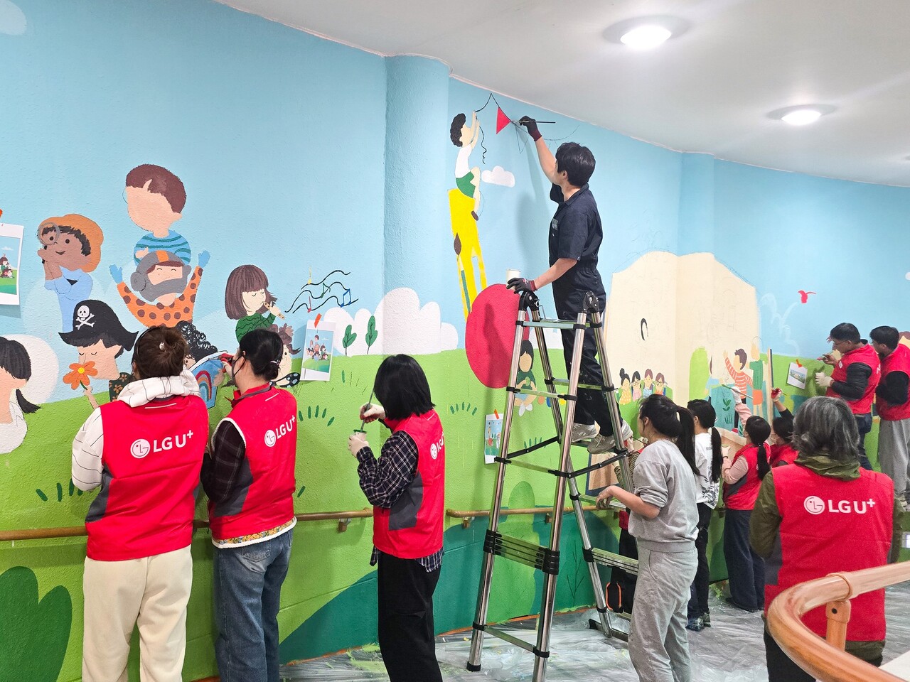 LG유플러스 임직원들이 충주성모학교 담장에 벽화를 그리고 있는 모습/사진=LG유플러스